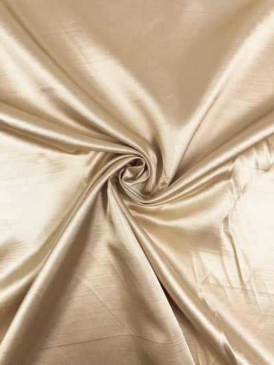 Super Cheap Fabrics' Shantung Satin in Gold (150cm) features a lustrous, light gold finish with smooth, gathered folds and a soft, reflective texture.