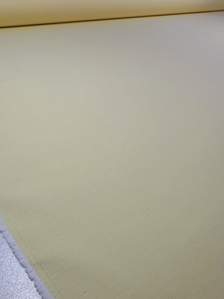 A large roll of Super Cheap Fabrics' Oxford Cotton - Lemon (146cm wide) is neatly spread out on a flat surface, with the rolled material visible at the top.