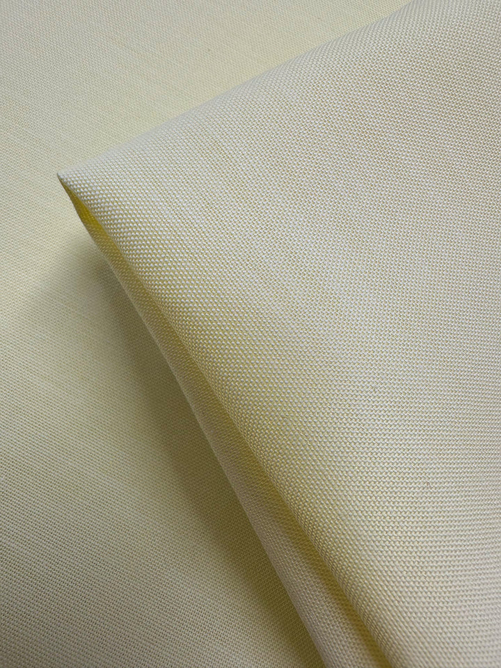 Close-up of Super Cheap Fabrics’ Oxford Cotton - Lemon (146cm) fabric, folded on a flat surface to highlight the detailed weave and texture of this cotton material.