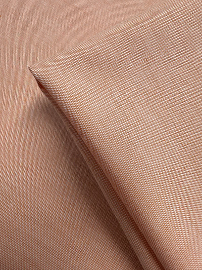 A close-up of Super Cheap Fabrics' Oxford Cotton - Sunburst (146cm) shows its light brown, finely textured weave. The light to medium weight fabric appears smooth with a subtle sheen and is shown folded on a flat surface.