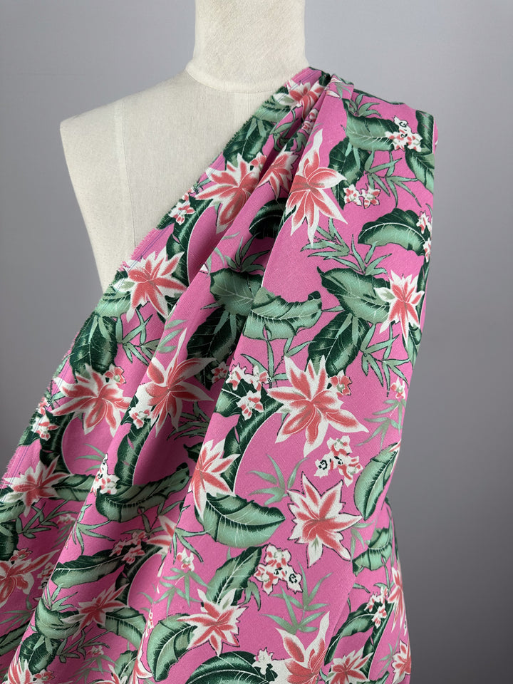 A mannequin showcases Super Cheap Fabrics' Printed Linen Blend - Jungle Bloom (140cm), a vibrant pink floral fabric with green leaves, set against a plain gray background.