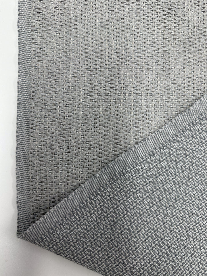 Close-up of Super Cheap Fabrics’ Upholstery - Bacchus Silver (145cm), a light gray woven fabric with a subtle textured pattern. One corner is folded to reveal the reverse, while neatly finished edges reflect its quality craftsmanship.