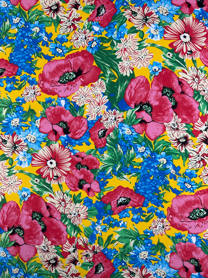 Designer Rayon - Sunset Bloom by Super Cheap Fabrics features large red and pink flowers, white blossoms, blue clusters, and green leaves on a bright yellow 145cm fabric—perfect for vibrant, energetic creations.
