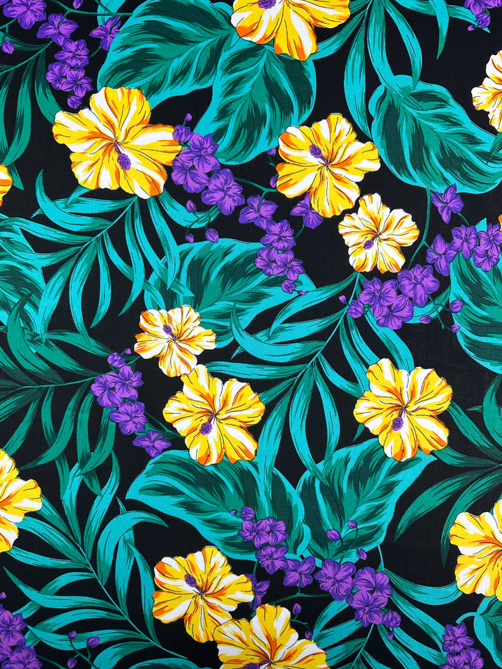 Super Cheap Fabrics' Designer Rayon - Neon Canopy - 145cm features yellow and orange hibiscus, small purple flowers, and green leaves on black—ideal for vibrant, lightweight projects.