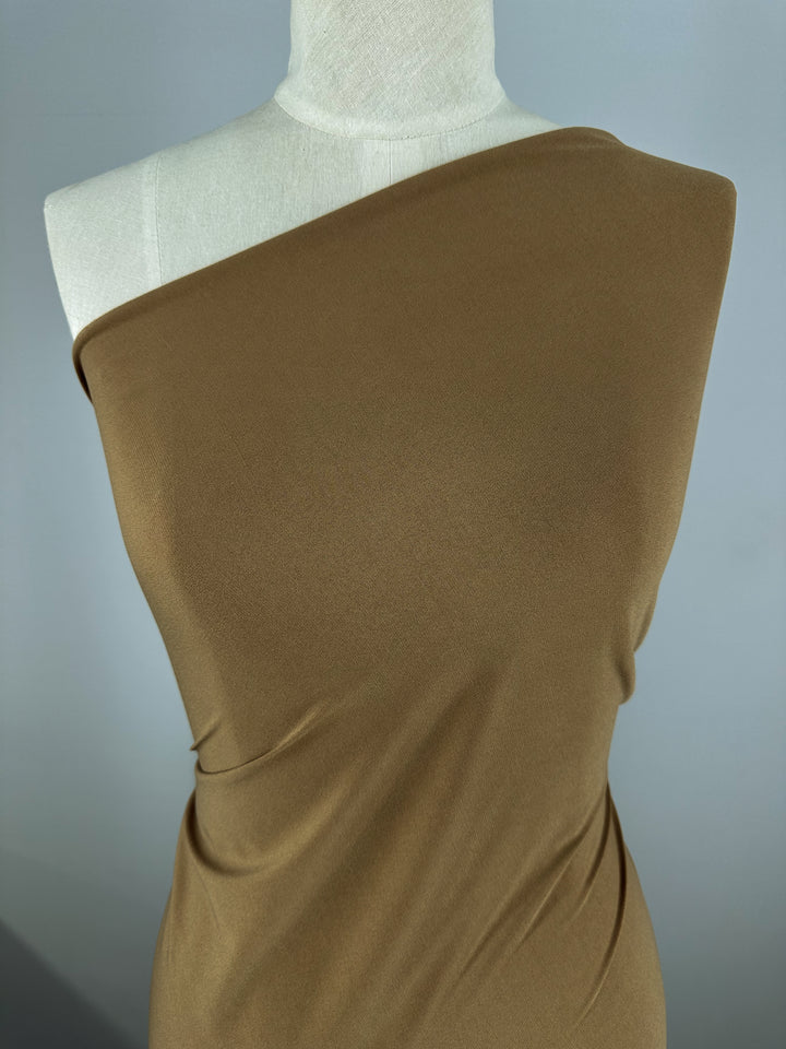 A dress form showcases Super Cheap Fabrics’ ITY Knit - Nuthatch - 150cm, a smooth brown polyester-spandex in a one-shoulder style, set against a plain gray background.