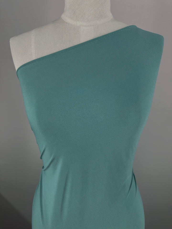 A dress form features Super Cheap Fabrics’ ITY Knit - Arctic - 150cm, draped to create an asymmetrical neckline exposing one shoulder, set against a plain gray background.