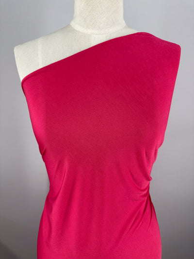 A mannequin displays the ITY Knit - Bright Rose - 150cm from Super Cheap Fabrics, a smooth, medium-weight fabric that drapes effortlessly and forms subtle folds, set against a neutral gray background.