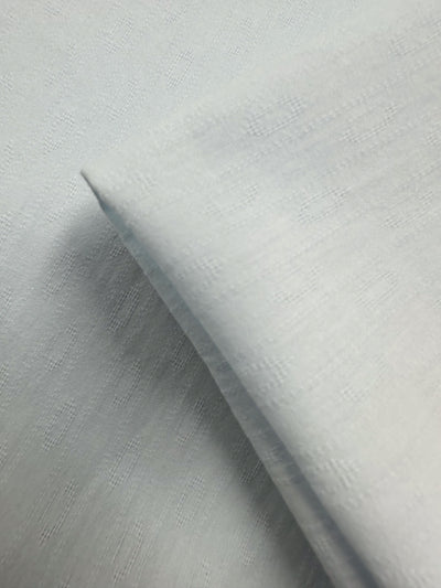Close-up of Super Cheap Fabrics’ Textured Cotton - Ice Melt (145cm), featuring light blue 100% cotton with a subtle diamond pattern, a folded section, and soft, smooth texture.