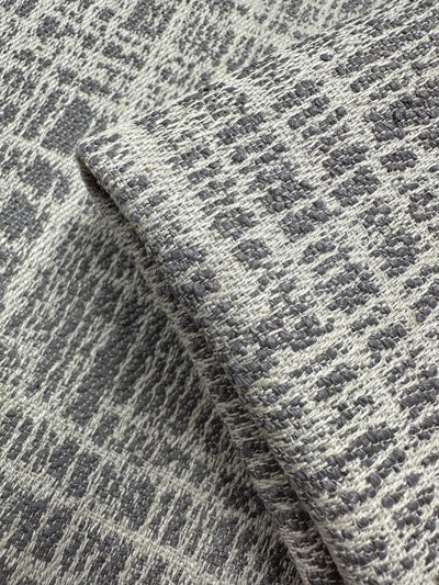 A close-up of Super Cheap Fabrics’ Textured Weave Upholstery - Dexter 33 Dove (147cm), showing its gray and white irregular geometric pattern, folded to display the fabric’s thickness and detailed weave.