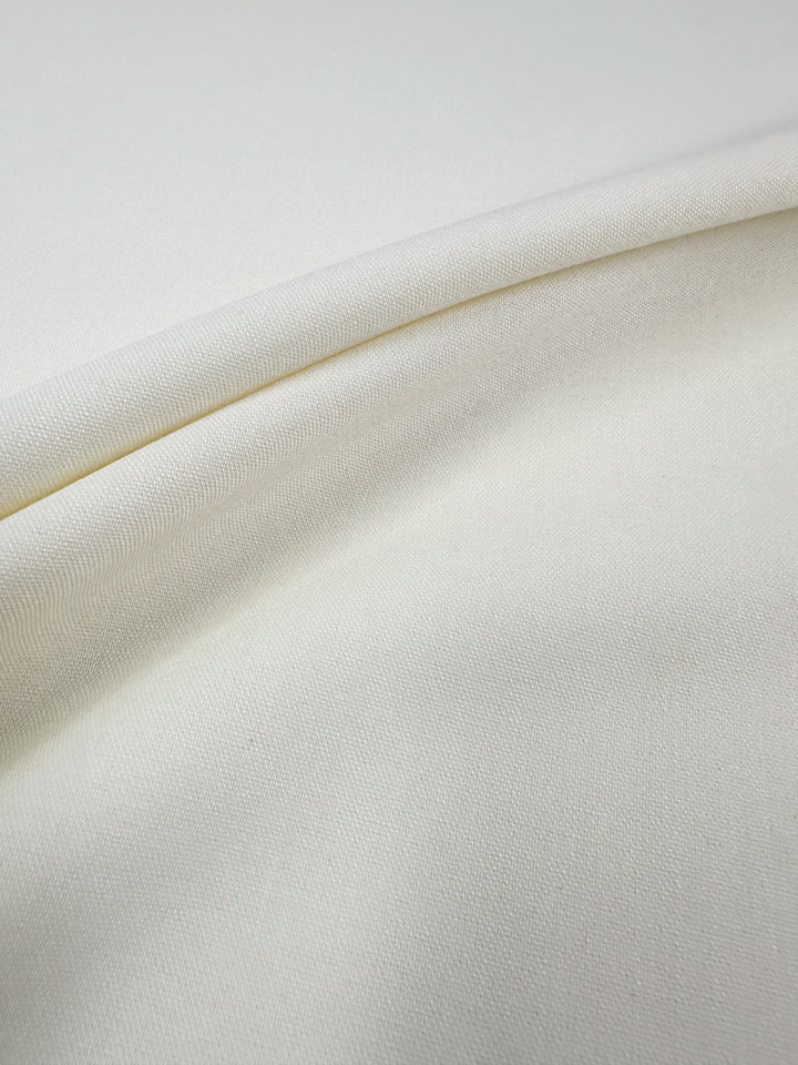 Close-up of smooth, off-white "Suiting - Pristine - 150cm" by Super Cheap Fabrics, featuring a subtle weave texture; this medium weight polyester viscose blend is ideal for tailored garments.
