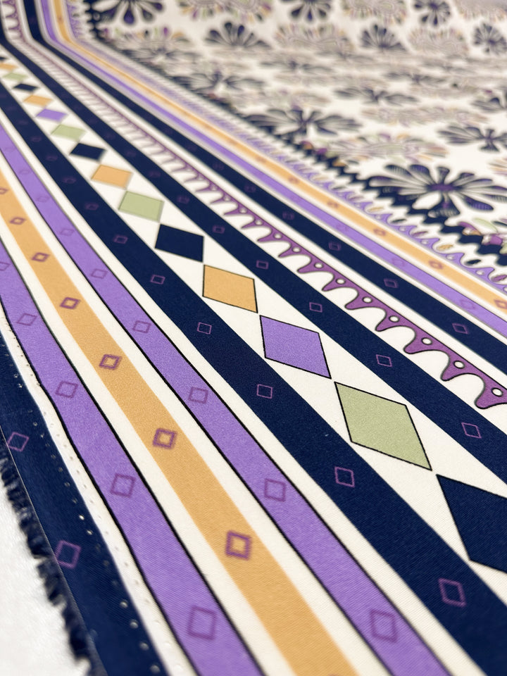 Designer Rayon - Lilac Tempo by Super Cheap Fabrics showcases vibrant diagonal stripes, diamonds, and floral motifs in purple, navy, yellow, green, and white on 145cm wide fabric in a close-up view.
