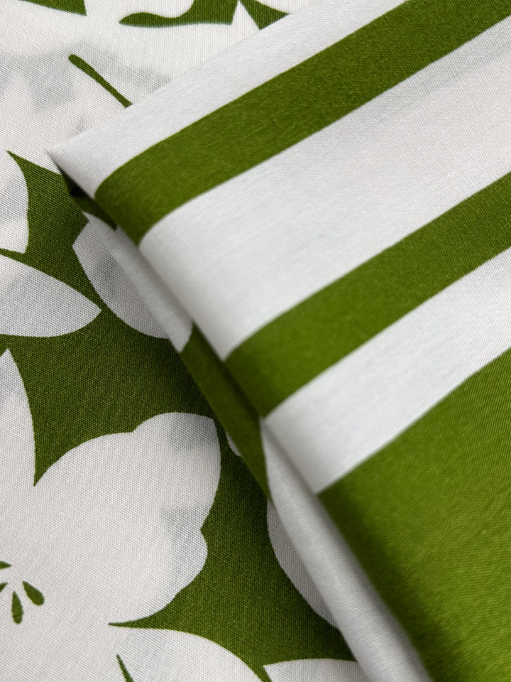 Close-up of Super Cheap Fabrics’ Designer Rayon – Olive Fade (145cm), featuring bold green and white stripes layered over a floral print with a white pattern on an olive background, highlighting the fabric’s vibrant design.
