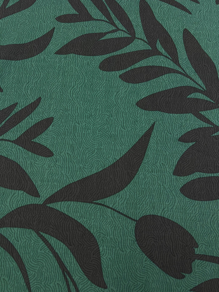 The Bamboo Rayon - Landscape - 152cm fabric from Super Cheap Fabrics is a green, lightweight material featuring a subtle wavy texture and a pattern of large, overlapping black leaves. Ideal for home decor, the varied shapes and sizes of the leaves create a dynamic contrast against the Bamboo Rayon background.