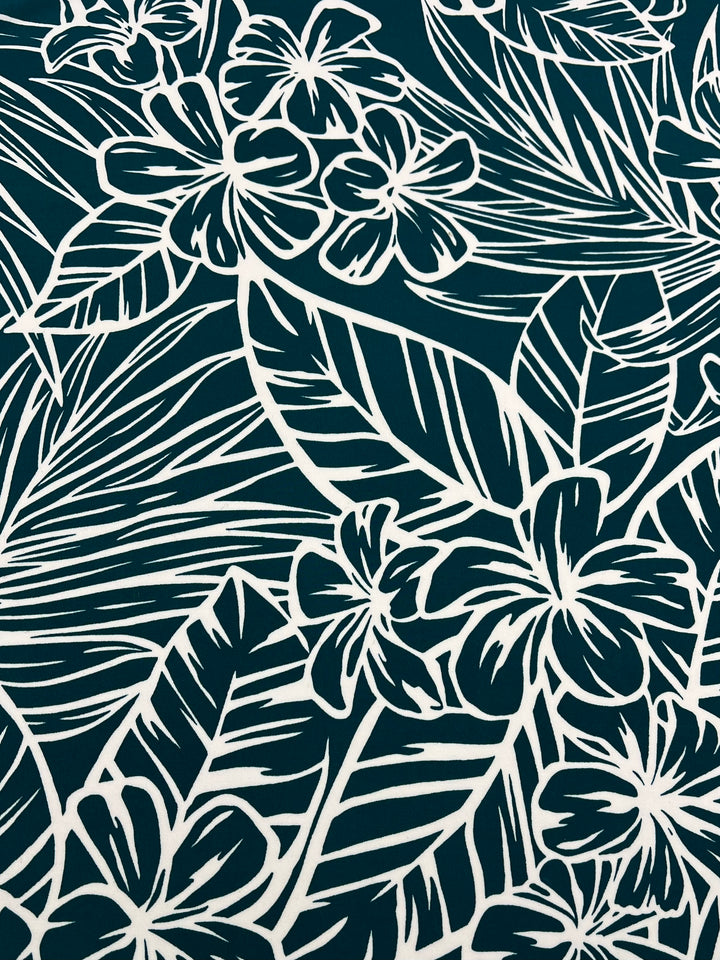 The Printed Lycra - Jasmint from Super Cheap Fabrics is adorned with an intricate pattern of white tropical flowers and leaves set against a dark green background. This design, printed on high-quality Polyester/Spandex fabric, features bold lines that outline the floral and leafy motifs, creating a lively and dense visual texture ideal for two-way stretch garments. The fabric width is 150cm.