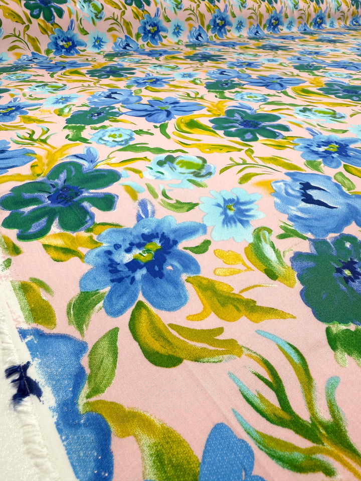 Super Cheap Fabrics' Designer Rayon - Bluebell Blush (145cm) features an organic feel and displays vibrant blue and green floral prints with yellow accents on a light pink background.