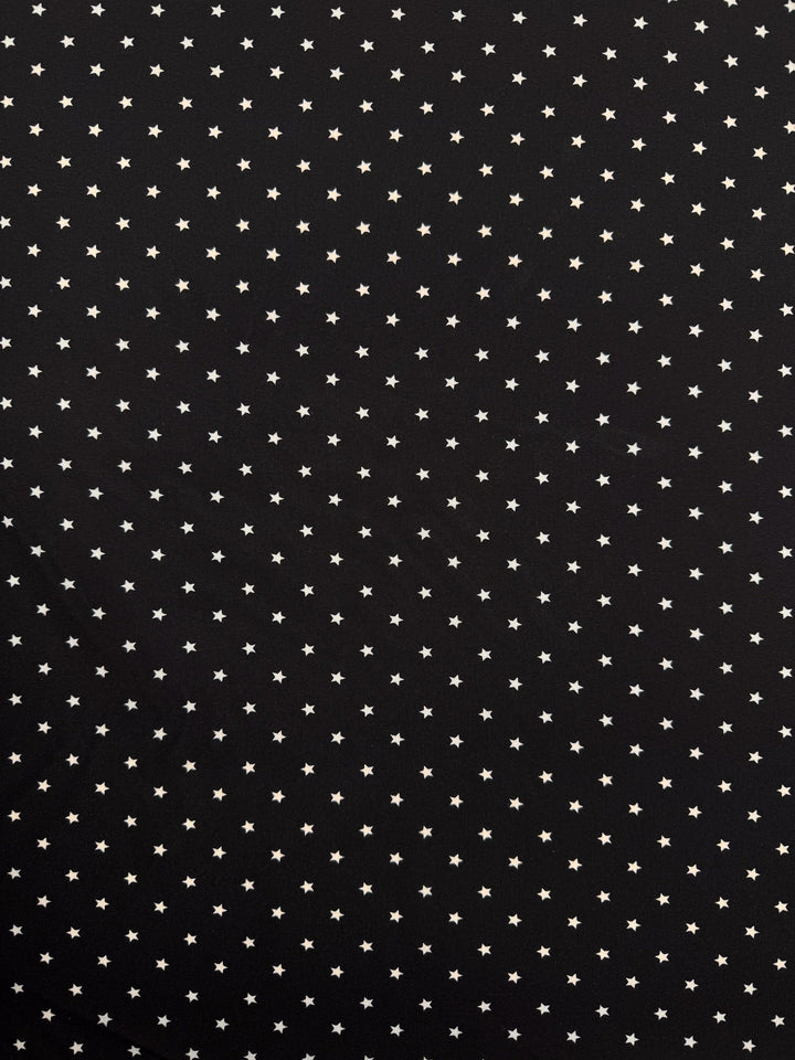 Super Cheap Fabrics' Stretch Chiffon - Comet (150cm) features a black background with small, evenly spaced white stars, creating a starry night sky effect—ideal for evening wear in extra lightweight polyester spandex.