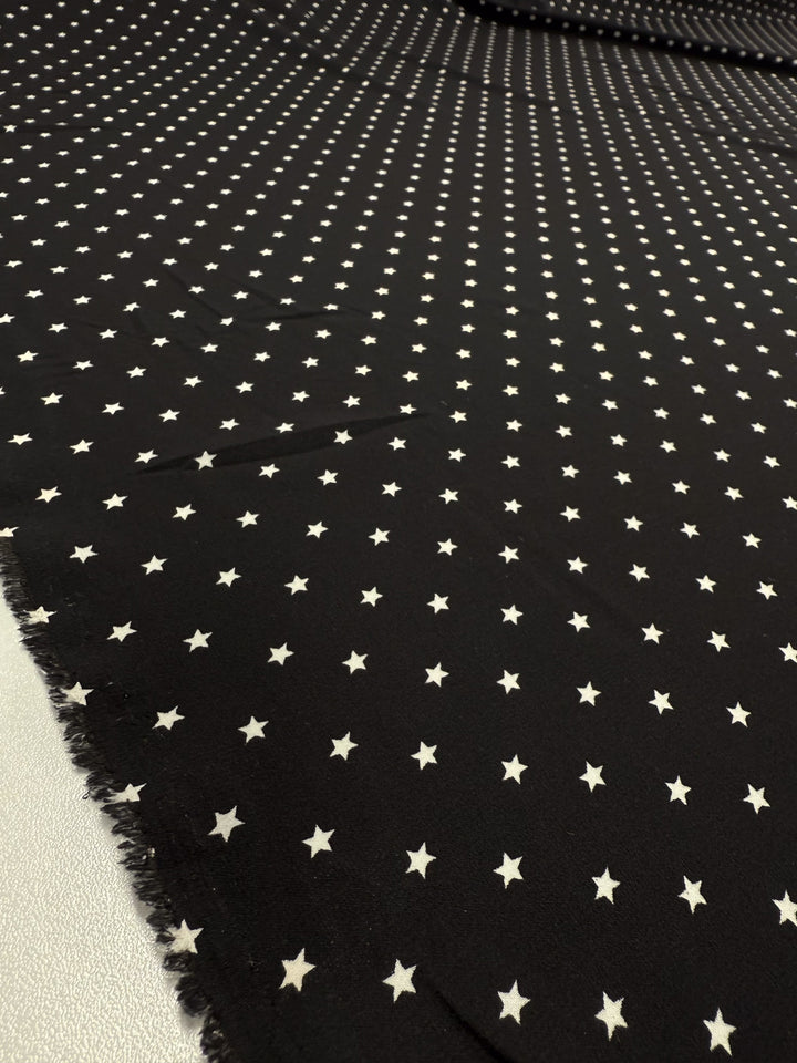Super Cheap Fabrics' Stretch Chiffon - Comet - 150cm is a black polyester spandex with radiant lines of small white stars, ultra-lightweight and ideal for evening wear. Edge is slightly frayed in the lower left corner.