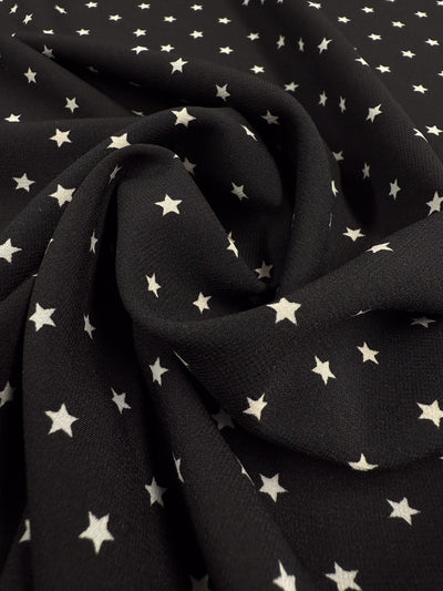 Super Cheap Fabrics’ Stretch Chiffon - Comet (150cm) is a black polyester spandex with small white stars, softly gathered and slightly wrinkled at the center—an extra lightweight fabric perfect for elegant evening wear.