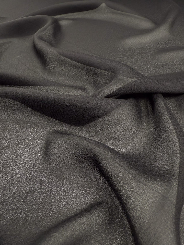Close-up of Super Cheap Fabrics’ Plain Georgette - Black - 114cm, a semi-sheer polyester fabric with a soft, flowing texture and subtle sheen, creating elegant movement and depth under the light.
