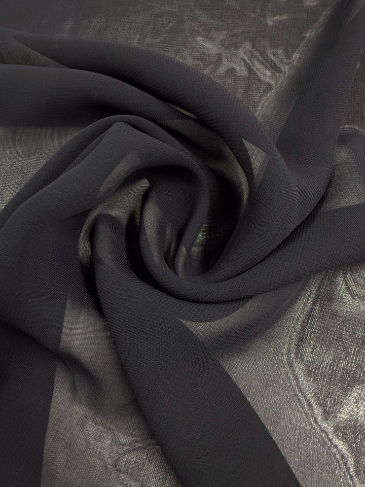 A piece of Single Georgette - Darkest Navy (143cm) from Super Cheap Fabrics arranged in a loose spiral on a shiny, textured silver surface.