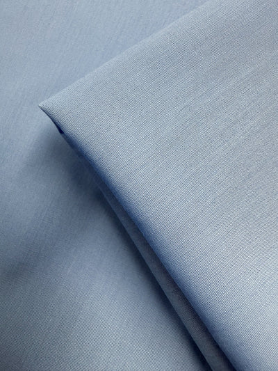 Close-up of Super Cheap Fabrics’ Poplin - Powder Blue - 114cm, a lightweight poly cotton fabric with a smooth texture and fine woven details, shown neatly folded and layered.