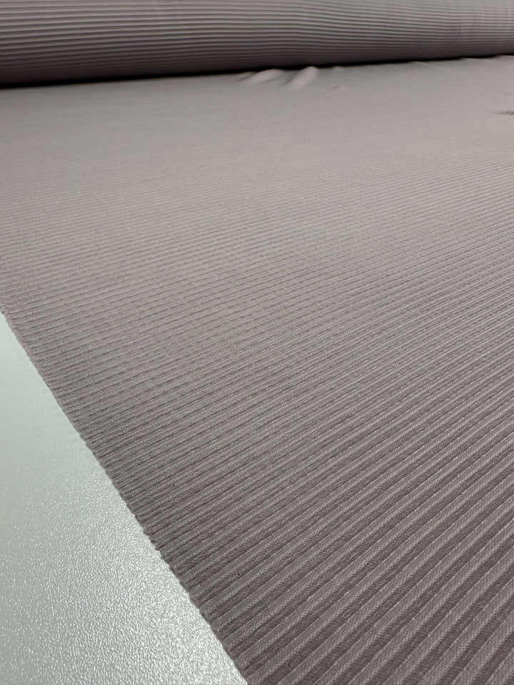 Close-up of Super Cheap Fabrics' Pleat - Violet Ice - 140cm, showcasing its textured gray polyester with parallel horizontal ridges. The lightweight material stretches into the background, suggesting a larger roll and highlighting its smooth uniform surface pattern.