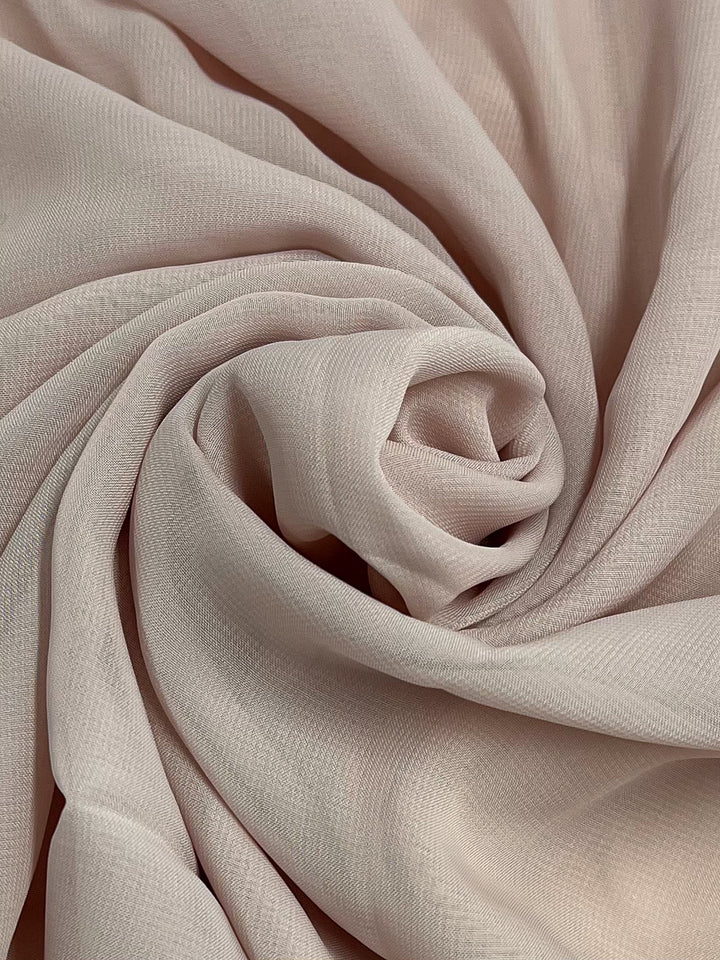 A close-up photograph of Super Cheap Fabrics' Hi-Multi Chiffon in Blush - 150cm intricately draped and folded in swirls, creating a soft, textured appearance. This lightweight fabric appears smooth and delicate, with subtle patterns visible on its surface.