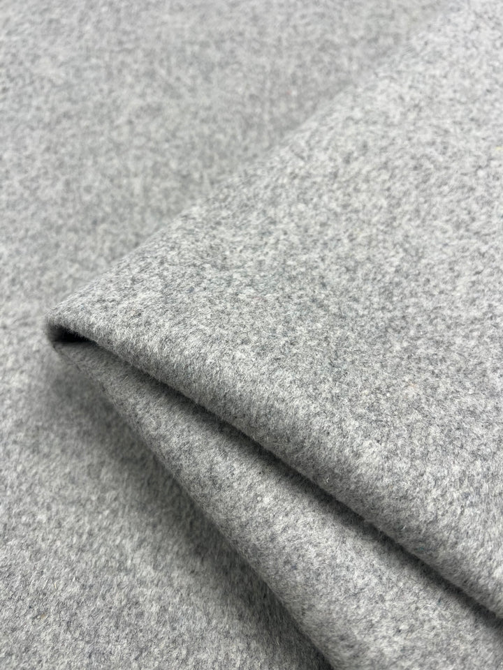 A close-up of a folded piece of Wool Cashmere - Grey Marle from Super Cheap Fabrics, showcasing its soft, woolen texture. The fabric displays a slightly heathered appearance with subtle variations in the grey tones and is dry clean only.