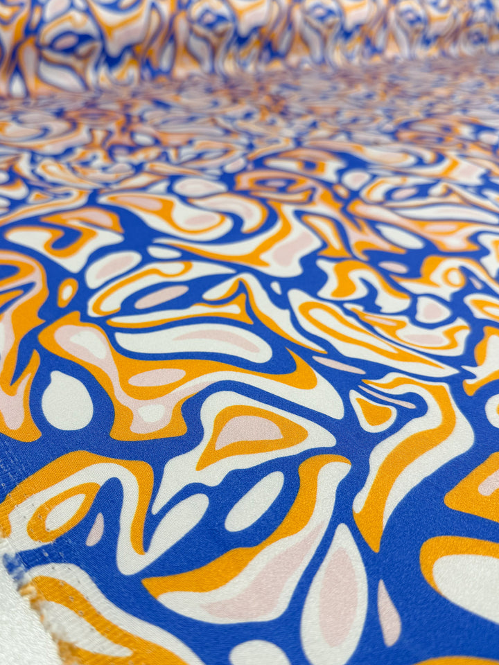 Close-up of Super Cheap Fabrics’ Mercerised Rayon - Electric Ember (145cm), featuring a lightweight fabric with a vibrant abstract pattern in blue, orange, white, and light pink swirls for a dynamic wavy design.