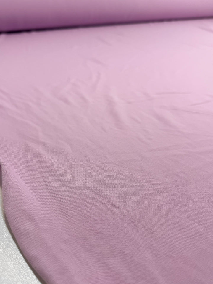 A close-up of Super Cheap Fabrics' Cotton Jersey - Orchid Bouquet - 165cm shows its soft light pink fabric, partially unrolled with gentle creases; its light to medium weight is ideal for comfy garments.