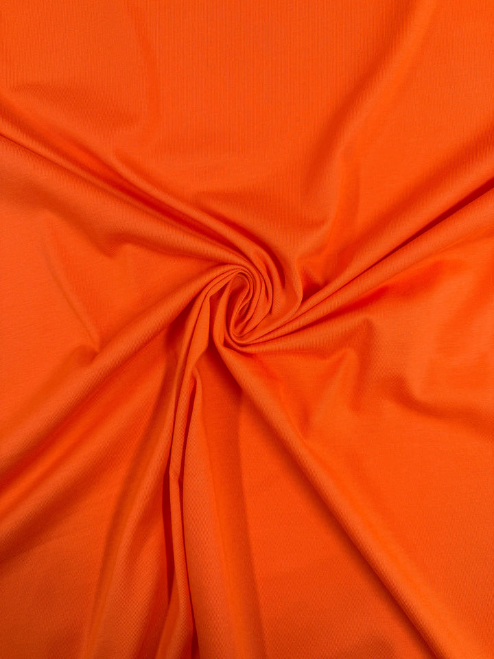 Super Cheap Fabrics’ Cotton Jersey - Mandarin Orange - 165cm is a lightweight, smooth fabric with vibrant color, featuring central gathering and radial folds—perfect for adding a bright touch to any project.
