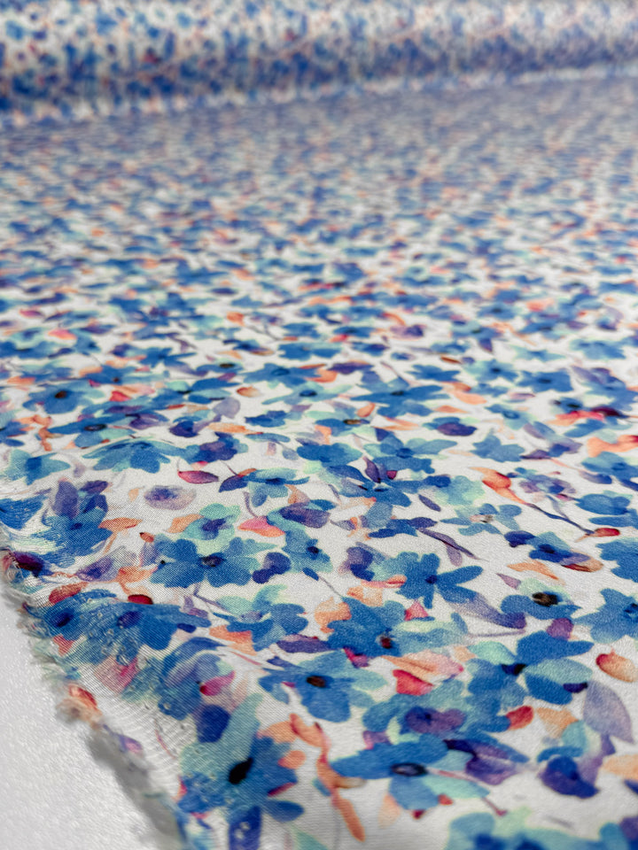 Close-up of Super Cheap Fabrics' Mercerised Rayon - Bluebell Drift (150cm), featuring a lightweight fabric with a vibrant blue, purple, pink, and orange floral pattern spread out on a flat surface.