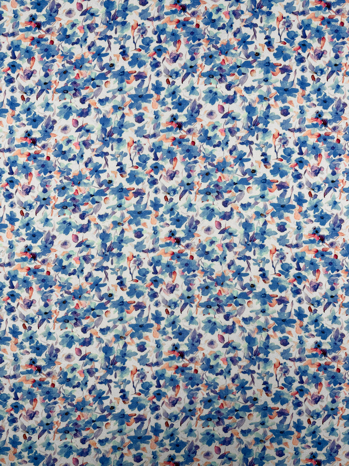 The Super Cheap Fabrics Mercerised Rayon - Bluebell Drift (150cm) showcases a lightweight rayon with a watercolor-style floral pattern in blue, purple, and orange on a densely covered white background.