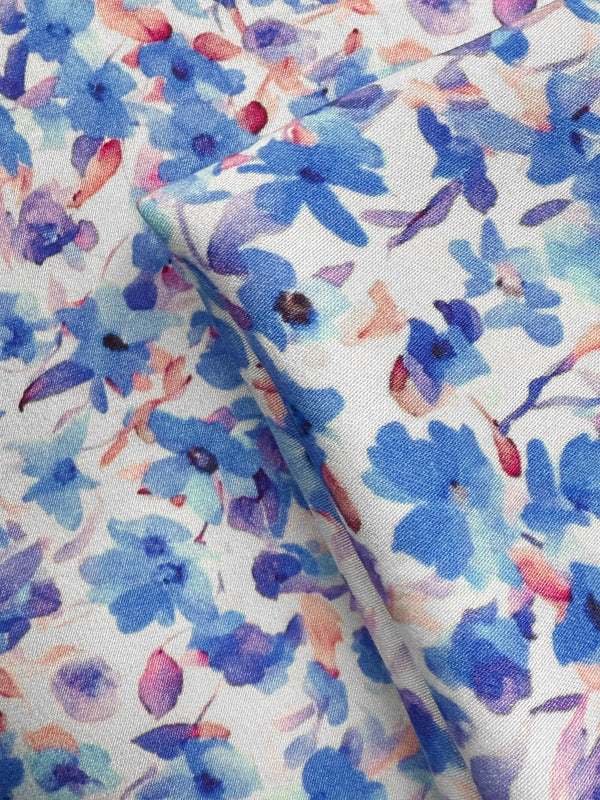 Close-up of Super Cheap Fabrics’ Mercerised Rayon - Bluebell Drift (150cm): lightweight, breathable material with a watercolor floral pattern in blue, purple, and pink on white, featuring soft overlapping flower shapes.