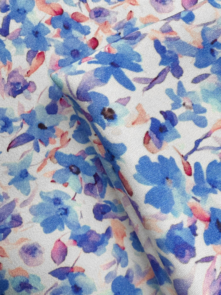 Close-up of Super Cheap Fabrics’ Mercerised Rayon - Bluebell Drift (150cm): lightweight, breathable material with a watercolor floral pattern in blue, purple, and pink on white, featuring soft overlapping flower shapes.