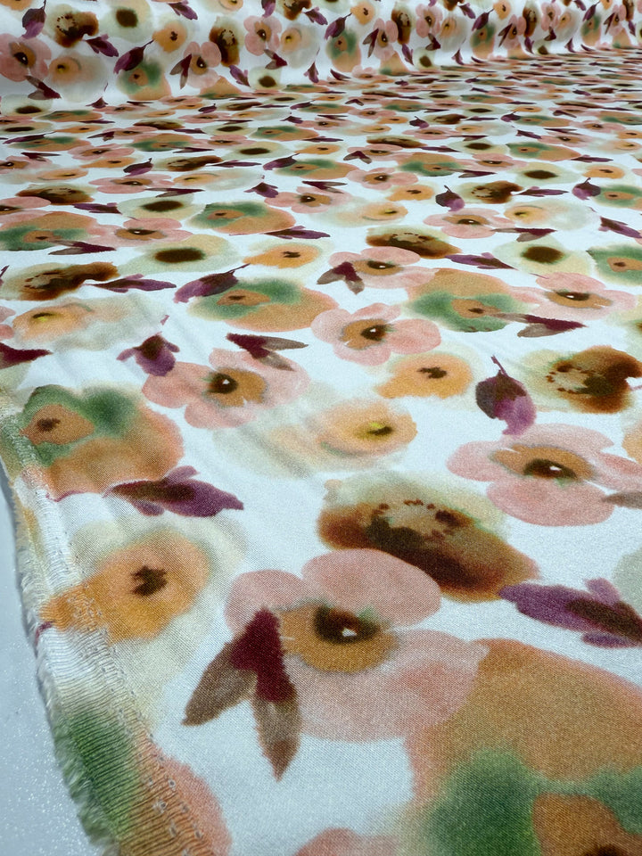 A close-up of Super Cheap Fabrics’ Mercerised Rayon - Blushed Camellia (150cm), a lightweight rayon with soft, watercolor-style pink, orange, green, and brown floral patterns on a light background spread smoothly on a flat surface.
