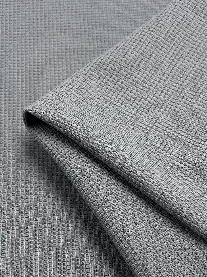 Close-up of Super Cheap Fabrics' Waffle Knit - Grey - 170cm, highlighting its soft material and intricate grid-like textured waffle pattern in light gray.