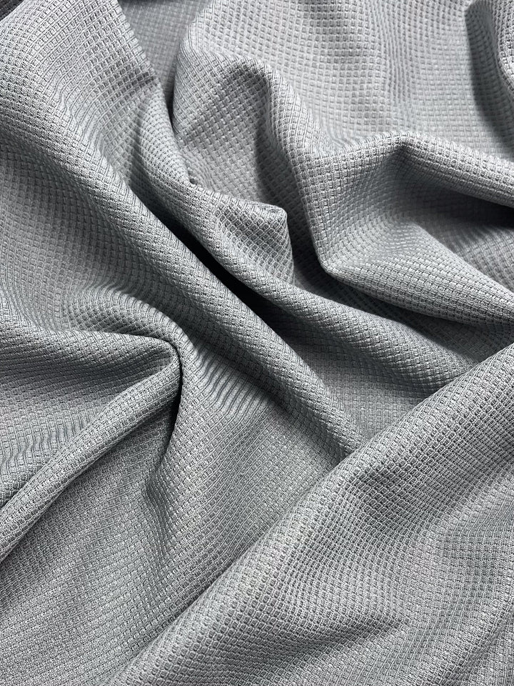 Super Cheap Fabrics' Waffle Knit - Grey - 170cm features a light gray waffle texture, shown draped and softly wrinkled to showcase its unique pattern and folds.