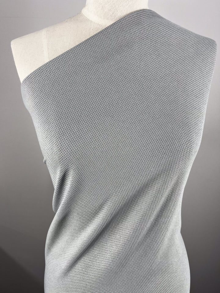 A dress form draped in Super Cheap Fabrics' Waffle Knit - Grey - 170cm, featuring textured fabric wrapped diagonally over one shoulder for an asymmetrical, off-the-shoulder style.