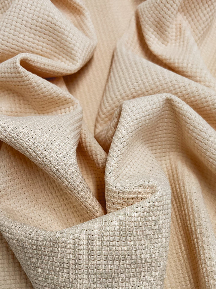 Close-up of the Waffle Knit - Sun Kiss by Super Cheap Fabrics, showing its beige waffle texture with soft folds. The honeycomb pattern creates a dynamic play of light and shadow across its 170cm wide three-dimensional surface.