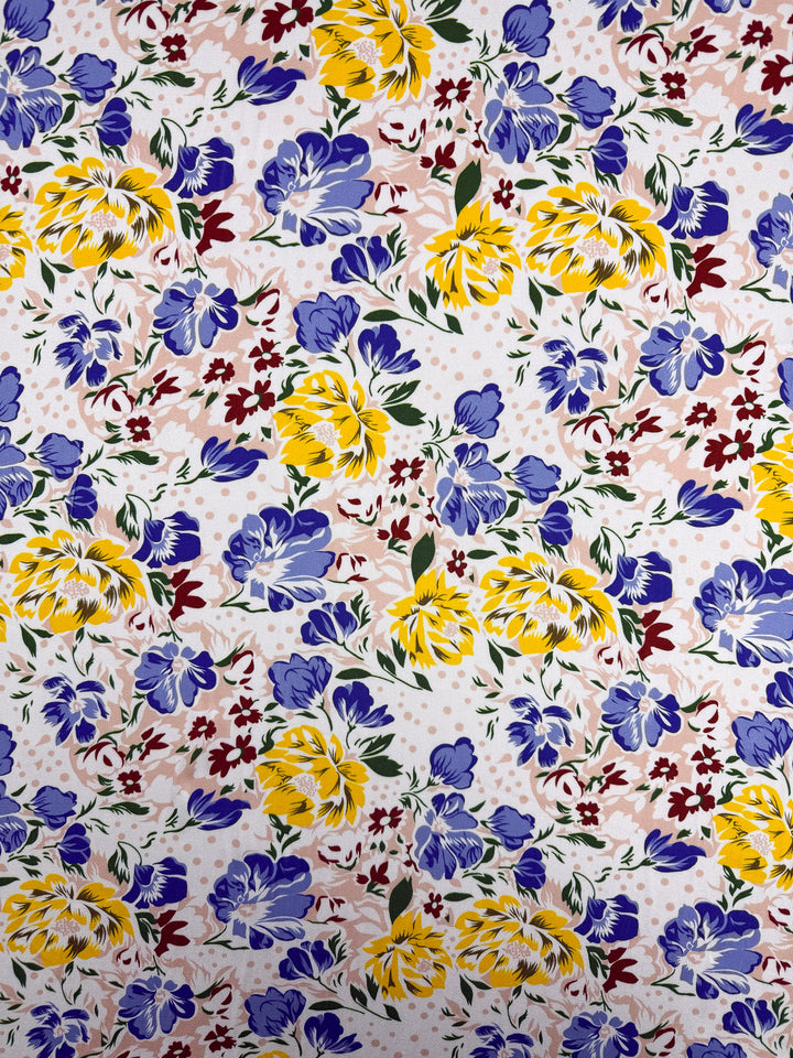 The Super Cheap Fabrics Mercerised Rayon - Spring Bouquet (150cm) features a vibrant floral print with yellow and blue flowers, green leaves, red details, and a light pink-on-white background, crafted from breathable fabric for all-day comfort.