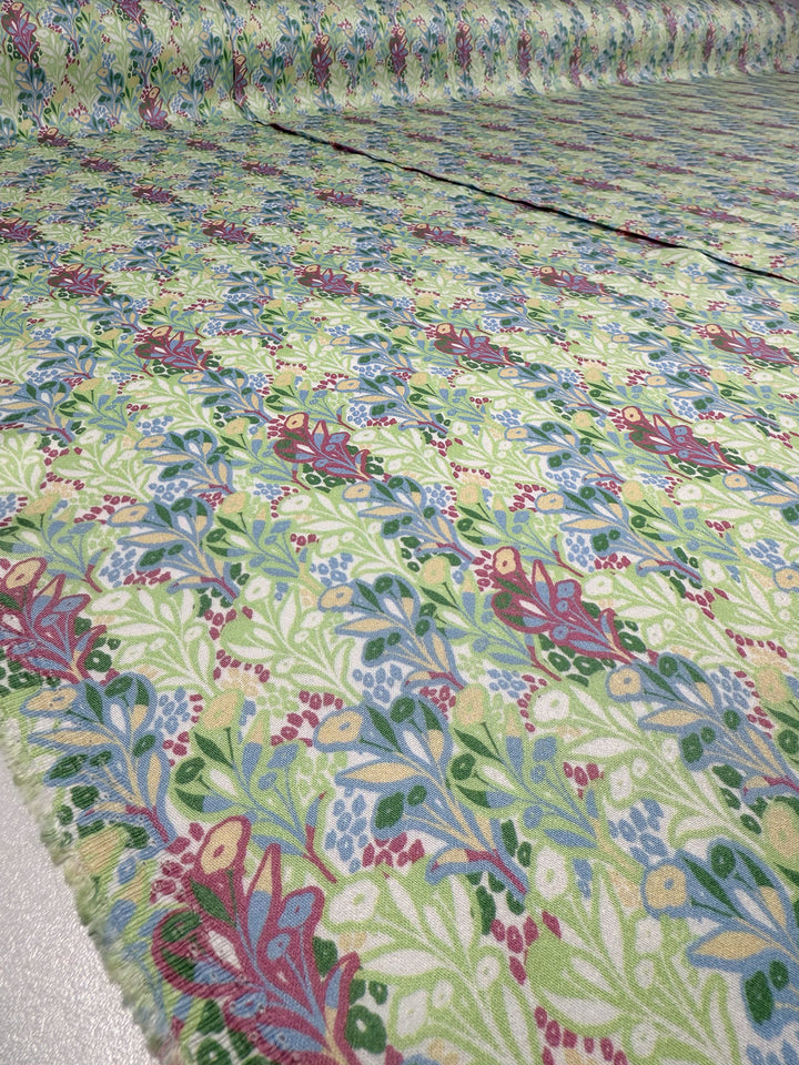 A close-up of Super Cheap Fabrics' Mercerised Rayon - Garden Vine (150cm), featuring a vibrant green, red, blue, and yellow floral and leafy pattern displayed on a flat surface.
