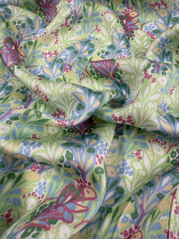 A close-up of the Mercerised Rayon - Garden Vine fabric by Super Cheap Fabrics shows its colorful, breathable floral and leafy pattern in green, blue, red, and beige on a softly wrinkled, textured 150cm lightweight rayon textile.