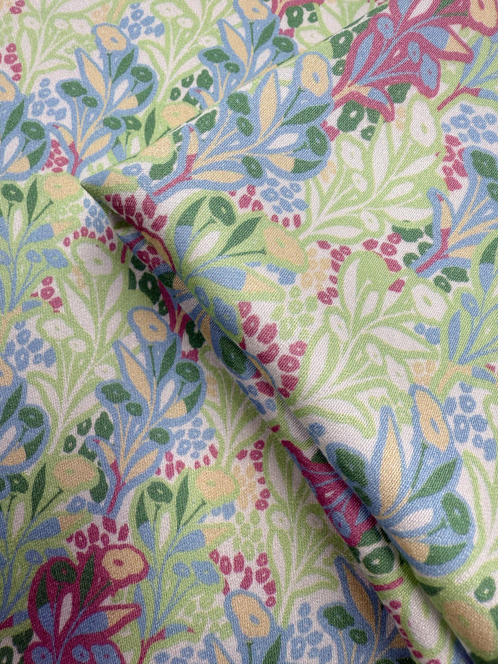 Close-up of Mercerised Rayon - Garden Vine (150cm) by Super Cheap Fabrics, featuring breathable rayon with a colorful floral pattern of green leaves, blue and yellow flowers, and red berries on a light background.