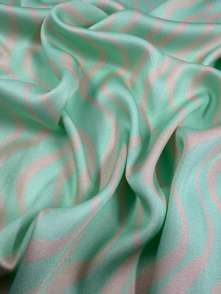 A close-up of Super Cheap Fabrics’ Mercerised Rayon - Seafoam Rhythm (150cm) shows its light green, wavy cream pattern and softly crumpled, smooth texture—perfect as a lightweight, breathable fabric.