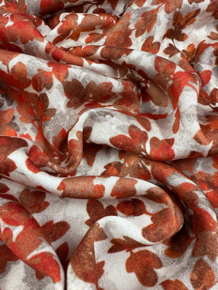 A close-up of Mercerised Rayon - Crimson Canopy by Super Cheap Fabrics, a lightweight, breathable fabric featuring red and brown autumn leaves on a white background with a soft, slightly textured finish. Width: 150cm.