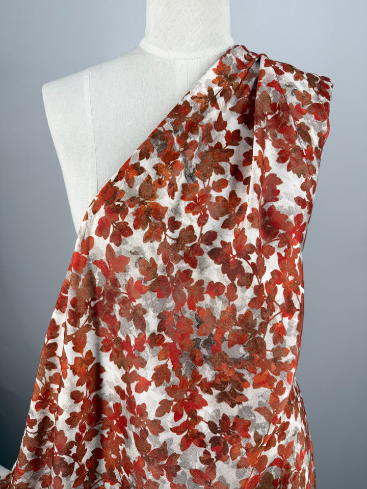 A white mannequin showcases Super Cheap Fabrics’ Mercerised Rayon - Crimson Canopy (150cm), featuring lightweight fabric with red, brown, and orange floral prints on white, set against a plain light gray backdrop.