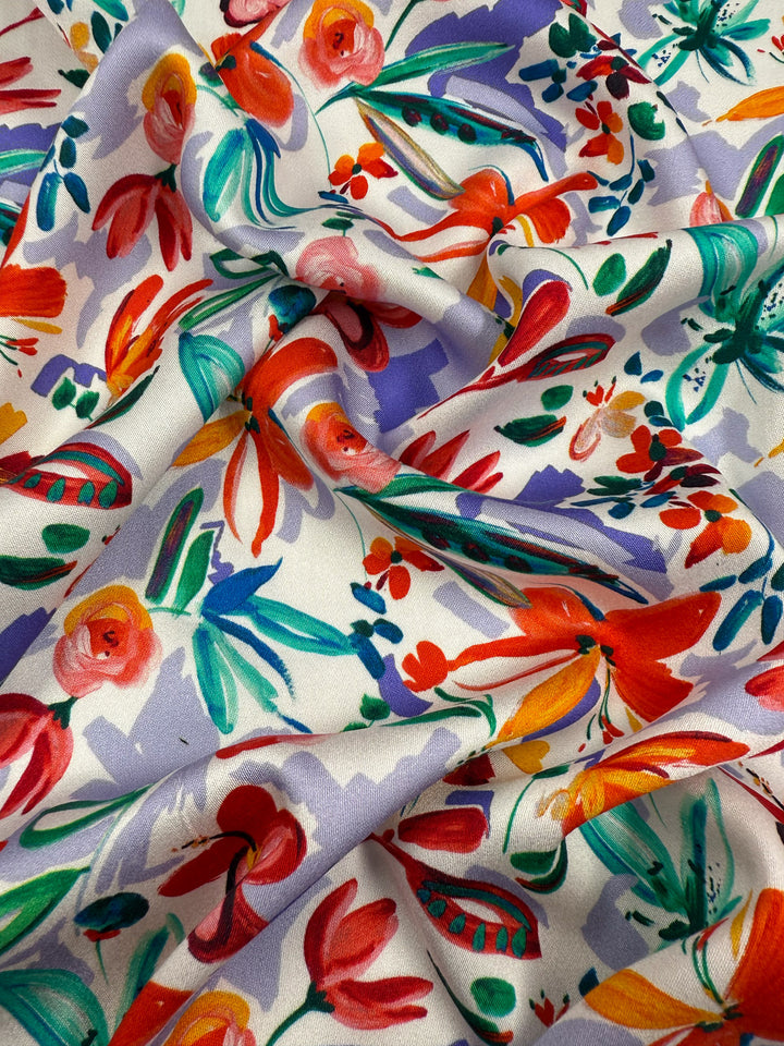 Super Cheap Fabrics' Mercerised Rayon - Tropical Brushstroke (150cm) features a colorful, breathable fabric with a vibrant hand-painted floral pattern in red, orange, green, purple, and pink blooming on a white background.