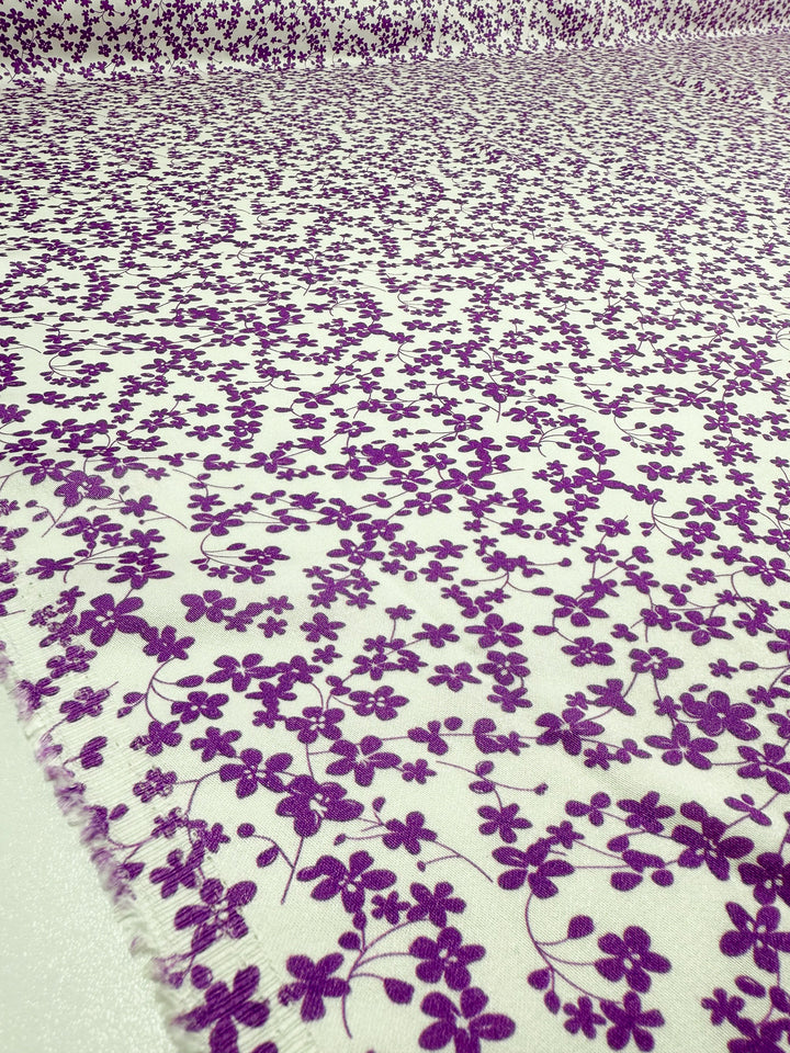Mercerised Rayon - Violet Meadow by Super Cheap Fabrics is a white, breathable fabric featuring densely scattered purple flowers and vines. Vibrant floral design with slightly frayed edges. Width: 150cm.