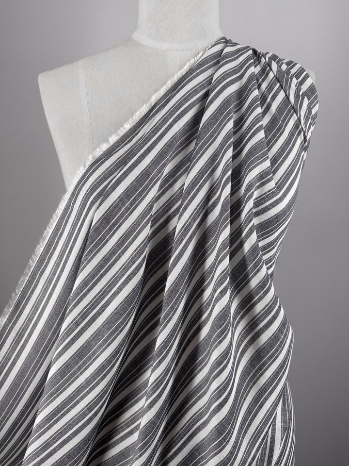 A mannequin showcases Super Cheap Fabrics' Linen Blend - Linen Stripe (150cm), a lightweight fabric in bold black and grey-white stripes, elegantly draped over one shoulder against a plain gray background.